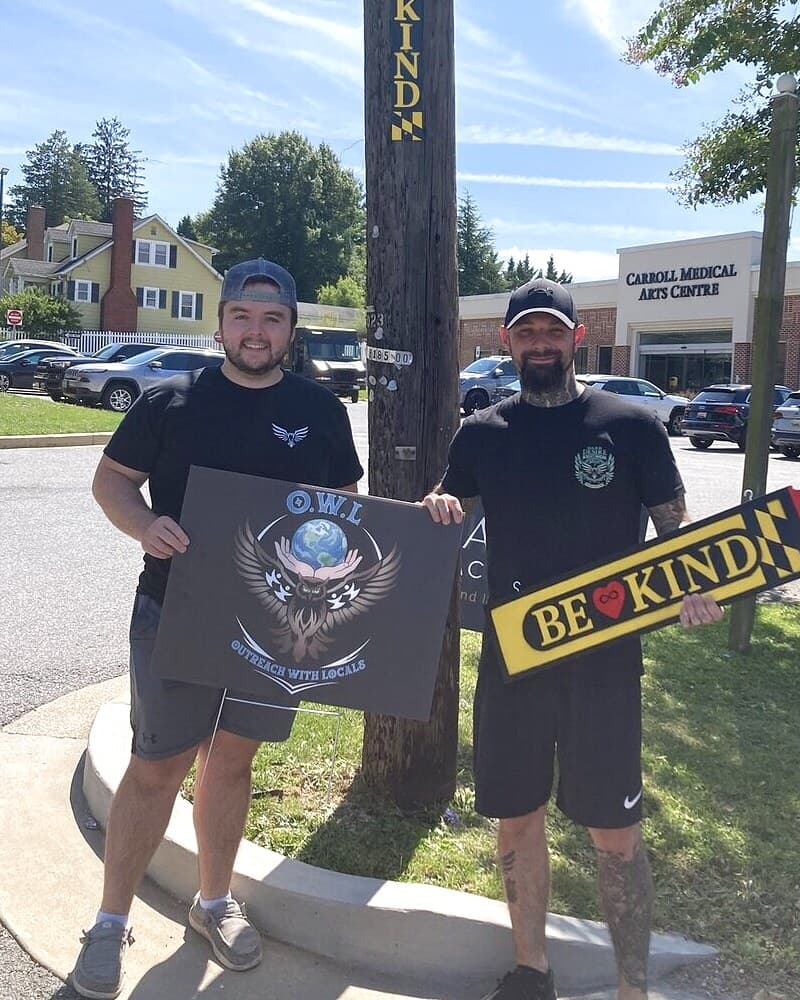 Jeremy Poe and Ryan Roberts of The OWL Movement on a Westminster street corner, Jeremy holding our sign and Ryan holding a Be Kind sign