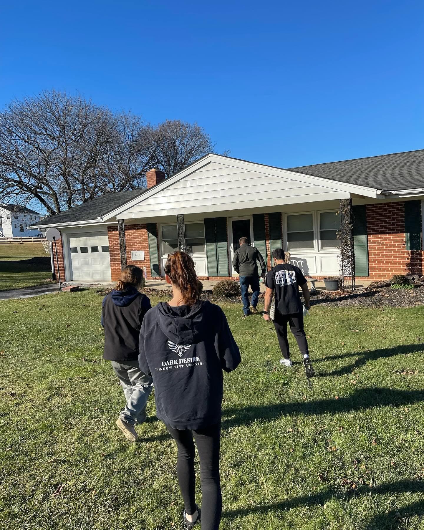 3 people crossing a lawn toward a house, one in a Dark Desire hoodie
